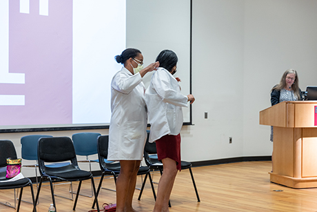 one Physician Assistant student putting a coat on another student