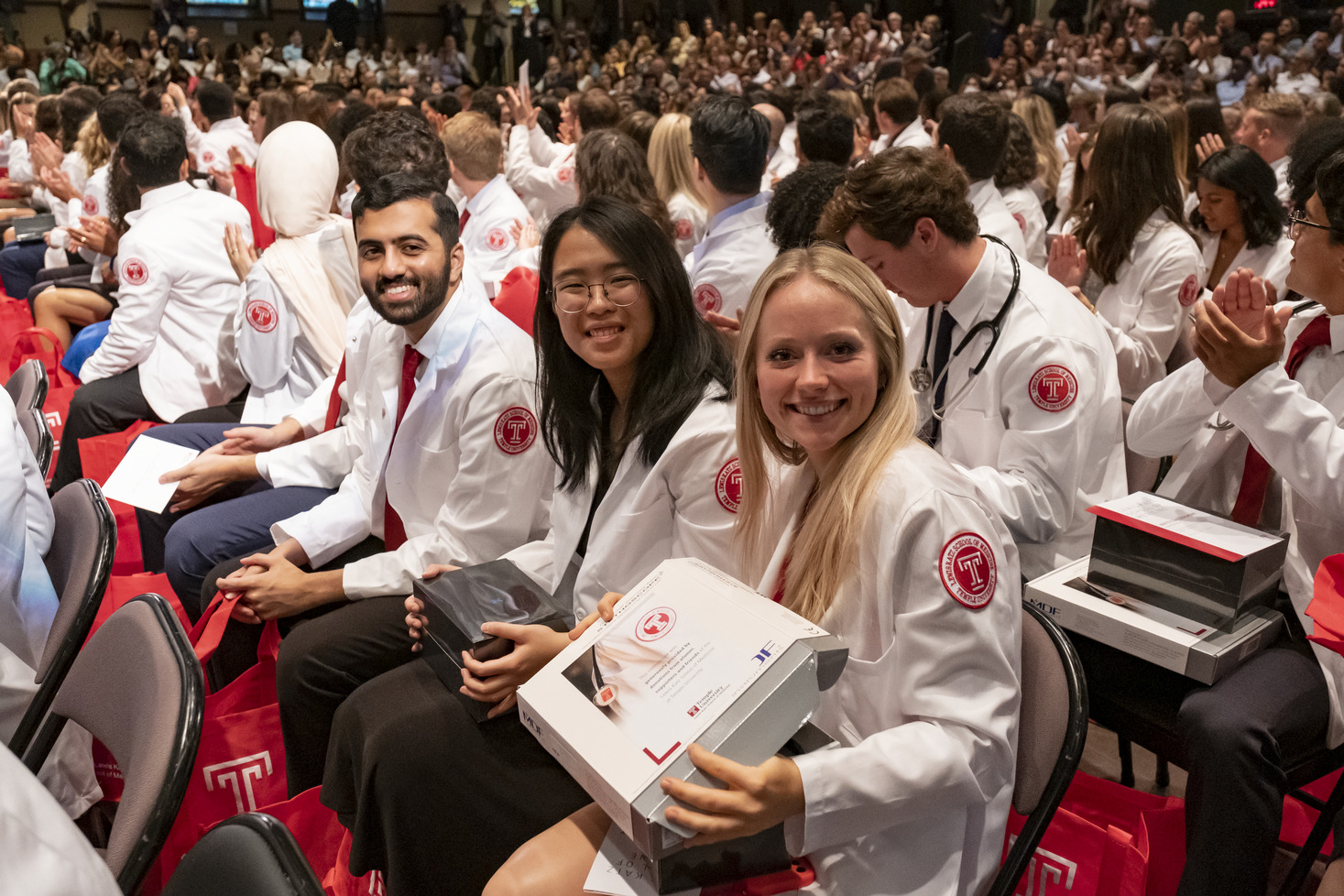 A smiling student holding her POCUS device in a large group of students sitting in the audience