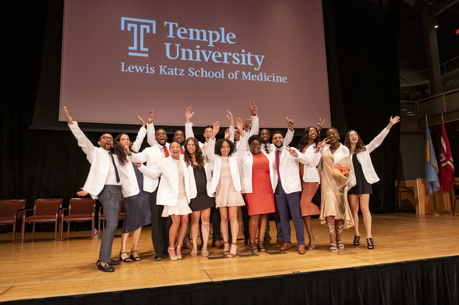 White-coated medical students are waving enthusiastically on the podium