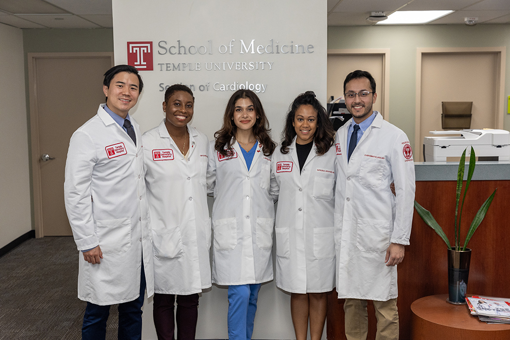Third-year Fellows in white coats, 2 men and 3 women, smiling