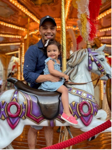 Dr. Francis Navarra with his young daughter sitting on a carousel horse