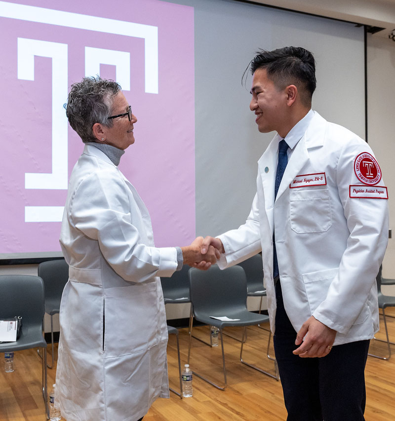 Dean of school shaking hands with student wearing a white coat