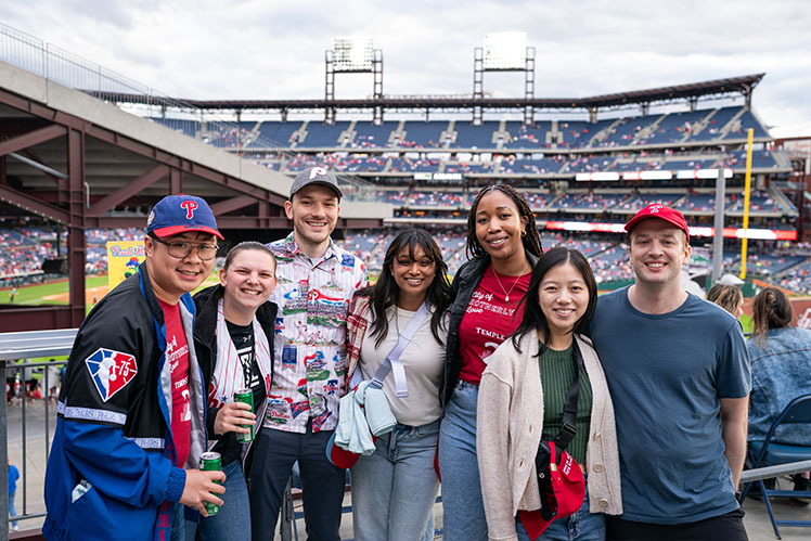 Group photo of alumni in front of a baseball field 