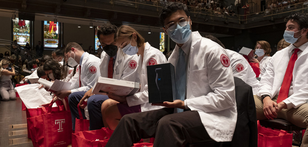 a Lewis Katz School of Medicine Class of 2026 student holding a point-of-care ultrasound (POCUS) device and Temple-branded stethoscope given to them at the Ceremony