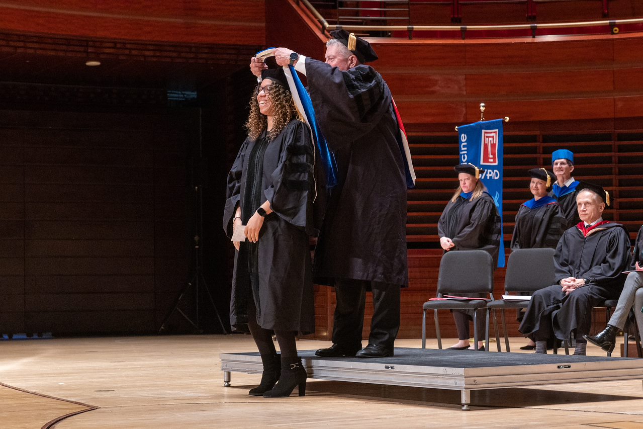 A smiling student receiving her graduation hood from a faculty member